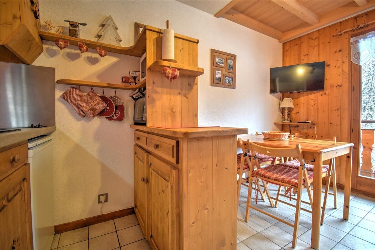 A cozy, rustic wooden kitchen and dining area in a chalet, featuring a dining table with chairs and a wall-mounted TV.