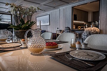 A beautifully set breakfast table in a luxury chalet, featuring fresh juice, a berry tart, orchids, and a view into the kitchen.