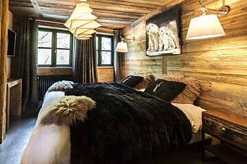 Rustic wooden bedroom with a cozy bed, faux fur accents, polar bear art, and unique lighting, evoking a warm, inviting chalet feel.