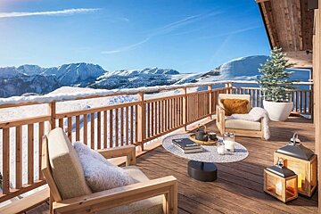 Cozy wooden chalet balcony with armchairs and lanterns, overlooking a scenic view of snow-covered mountains.