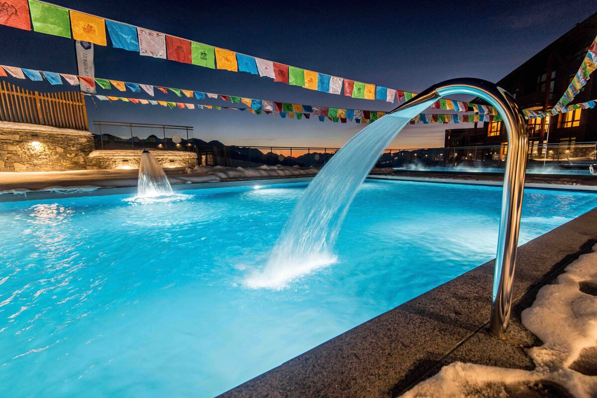 A swimming pool with a waterfall and flags hanging from the fence