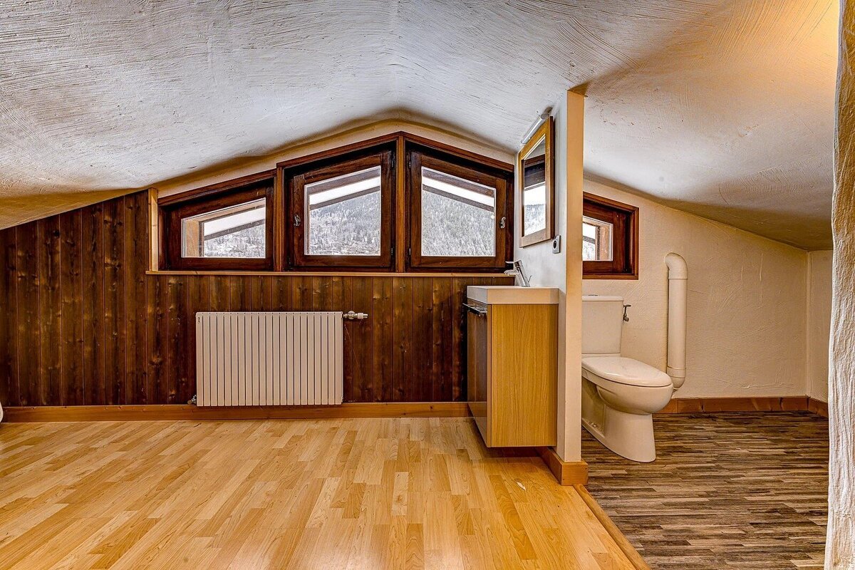 Attic bathroom with sloped ceiling, wood-paneled walls, mountain-view windows, radiator, sink, and toilet, featuring light and patterned wood floors.