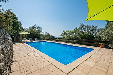 A large swimming pool surrounded by chairs and a green umbrella