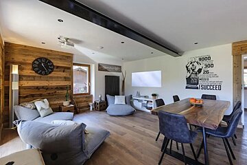 A modern living-dining space with wood-paneled walls, grey lounge chairs, a wooden dining table, and a Michael Jordan wall mural.