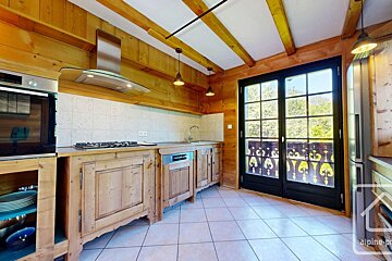 Cozy, rustic wooden kitchen with modern appliances, tiled floor, and a large glass door opening to a balcony with a scenic view.
