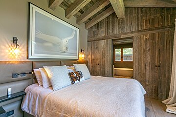 Cozy, rustic bedroom with a large bed, snowy owl art, exposed wood beams, and a modern en-suite bathroom visible through sliding doors.