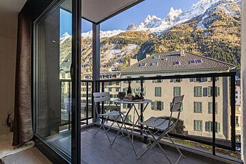A balcony with a table and chairs and mountains in the background