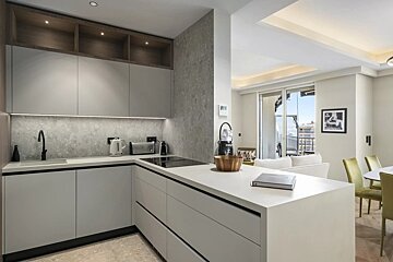 Modern open-plan kitchen with light grey cabinets, white counters, and a sleek island, opening to a living area with balcony views.