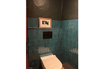 A bathroom with blue tiles and a picture on the wall above the toilet