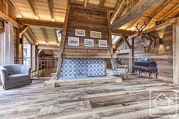 Cozy rustic cabin loft featuring a large wooden fireplace, exposed beams, a taxidermy deer head, and comfortable armchairs.
