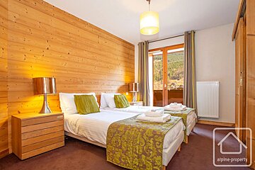 Cozy wooden-paneled bedroom with two twin beds and a glass door opening to a scenic mountain view.
