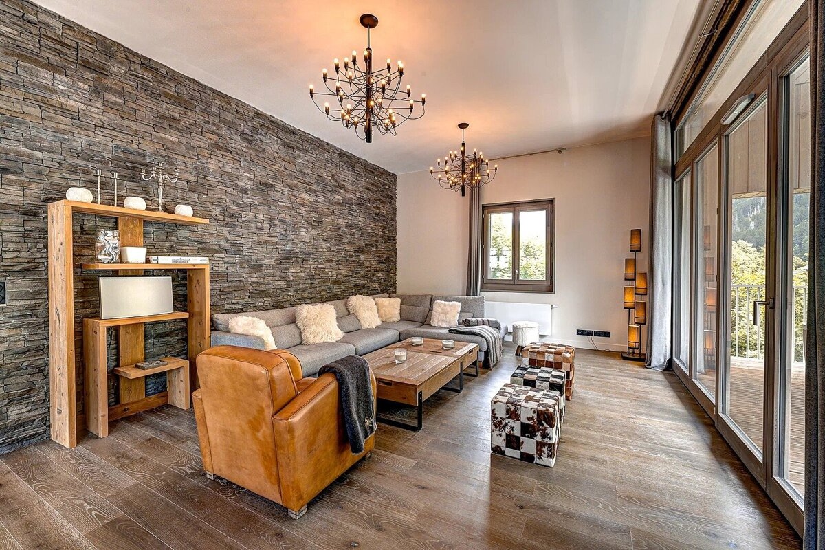Cozy living room with a stone accent wall, grey sectional, leather armchair, and large glass doors leading to a balcony.