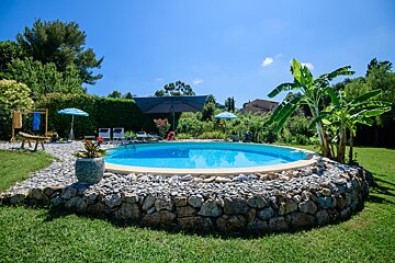 A swimming pool surrounded by rocks and umbrellas on a sunny day
