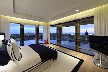 Modern bedroom with panoramic glass walls showcasing a beautiful landscape view at dusk. Navy and white decor with ambient lighting.