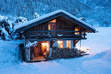 A snowy cabin with a balcony in the middle of a snowy forest