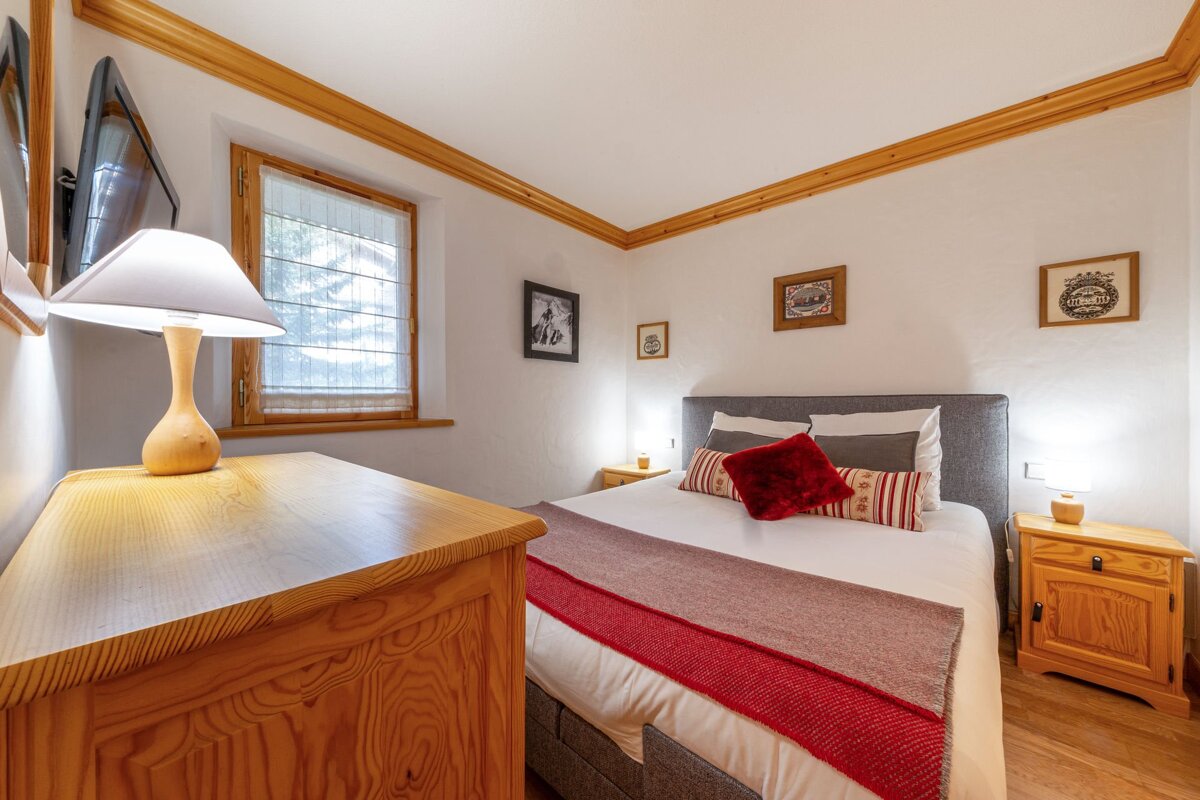 Inviting bedroom with a double bed, red throw, wooden dresser & nightstands, framed art, and a window providing natural light.