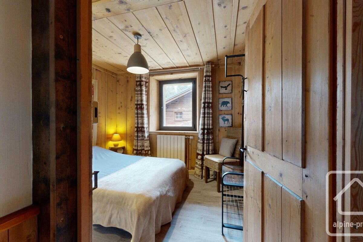 Cozy chalet-style bedroom with wood paneling, a bed, window, and rustic animal art, viewed from a doorway.
