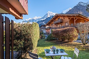 A table with a teapot and cups on it in front of a house with mountains in the background