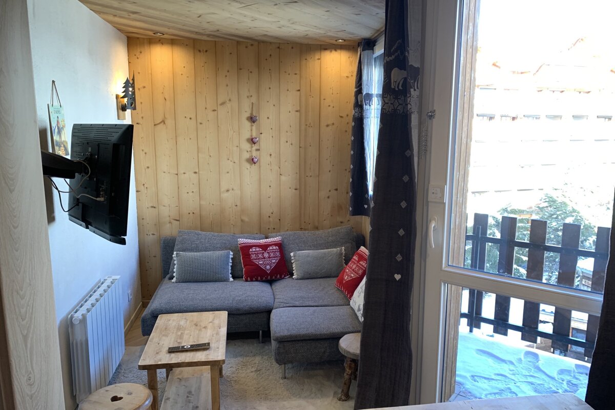 Cozy wood-paneled living area with a gray sectional sofa, TV, wooden coffee table, and a large window showing a snowy outdoor view.