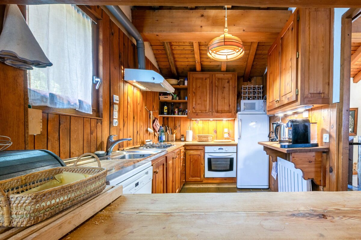 A rustic, all-wood kitchen with exposed beams, equipped with a sink, stove, fridge, oven, microwave, and a basket in the foreground.