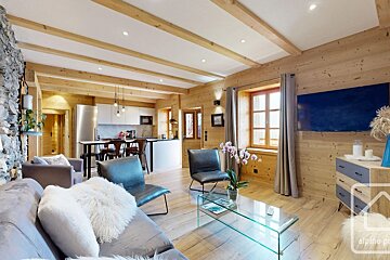 A bright, rustic-modern open-plan living room and kitchen featuring light wood, exposed beams, a stone wall, and contemporary grey furnishings.