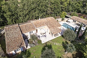 Aerial shot of a multi-building villa with tiled roofs, a private pool, and expansive patios, surrounded by dense trees and a green lawn.