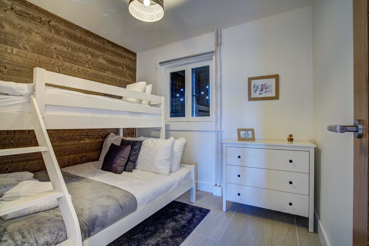 Cozy bedroom featuring white wooden bunk beds against a wood-paneled wall and a white three-drawer dresser.
