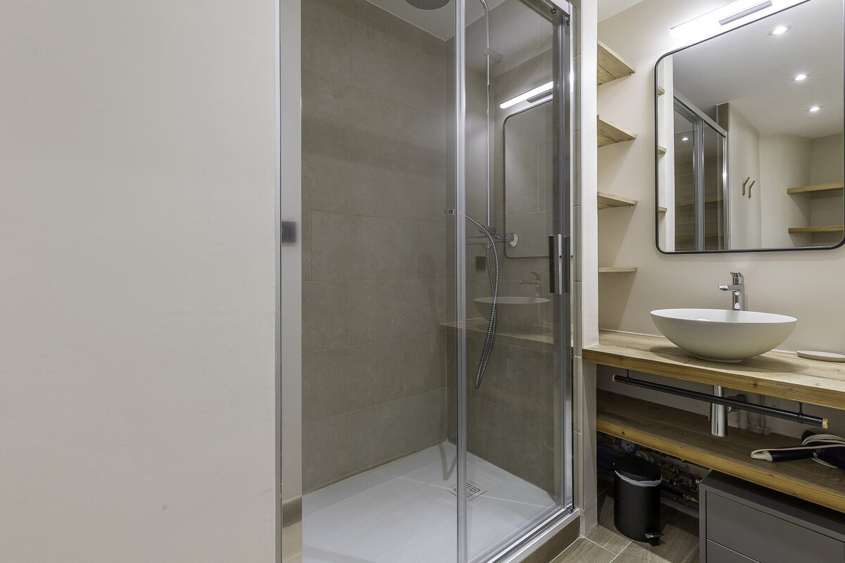 Modern bathroom with a glass walk-in shower, a wooden vanity with a vessel sink, and a rounded rectangular mirror.