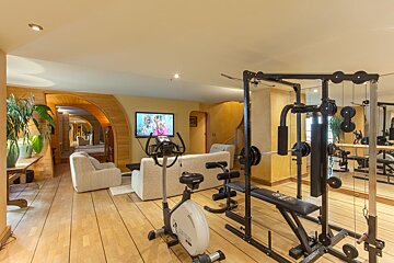 A modern home gym with an exercise bike and multi-station, seamlessly integrated into a cozy living area with a TV, sofa, and wooden arched doorways.
