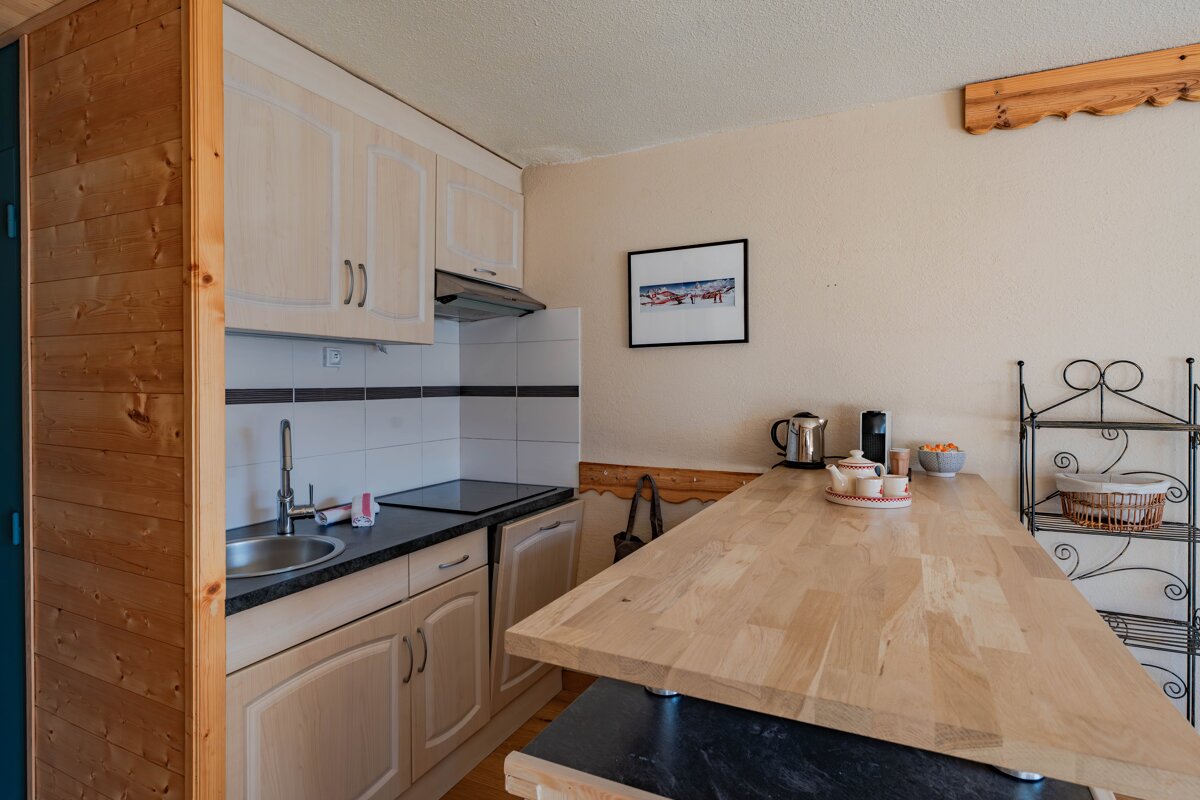A compact kitchen featuring light wood cabinets, a matching wooden breakfast bar, a sink, and a cooktop.