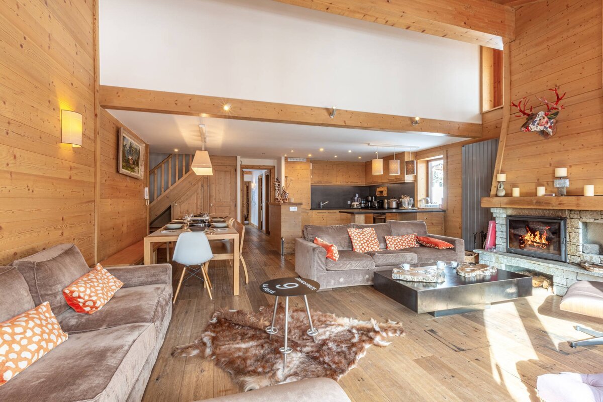 Cozy wooden chalet interior with a burning fireplace, comfortable sofas, and an open-plan dining and kitchen area.