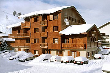 Snow covered cars are parked in front of a wooden building