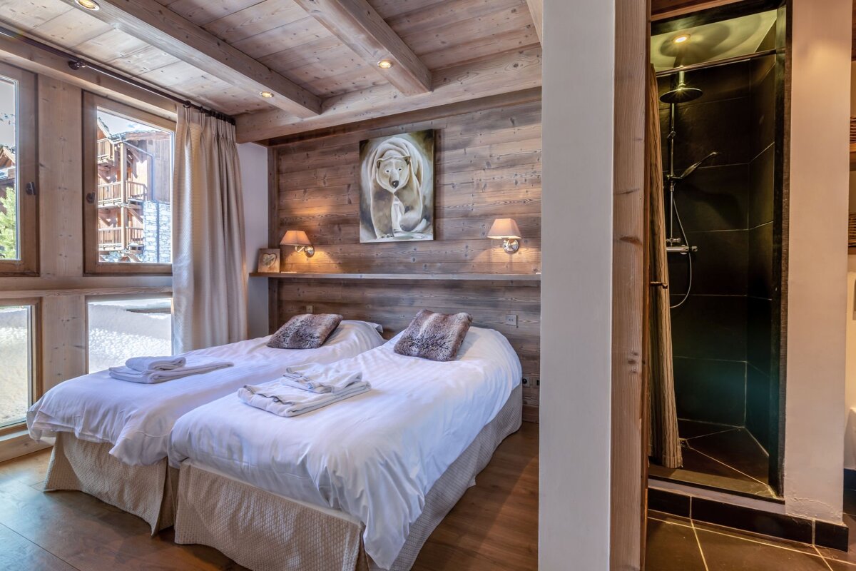 Rustic wooden chalet bedroom featuring twin beds, polar bear artwork, and a modern open shower to the right.