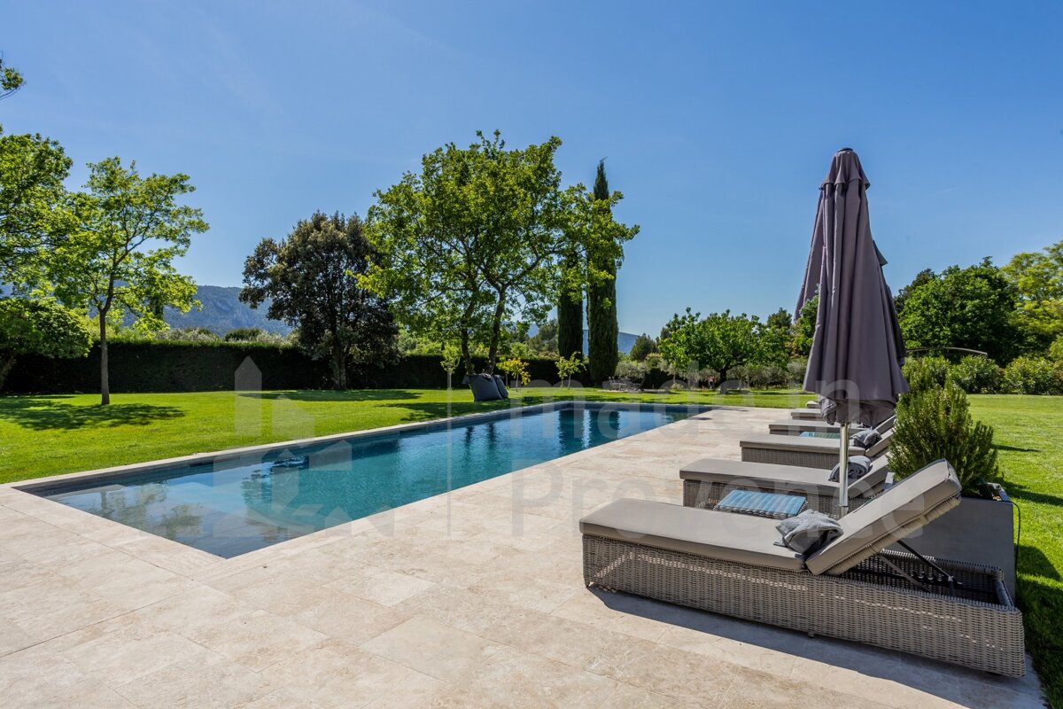 A large swimming pool is surrounded by lawn chairs and umbrellas