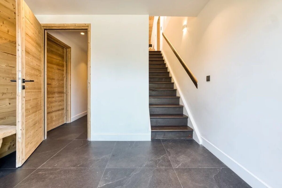Modern hallway featuring rustic wooden doors, dark tiled flooring, and a dark wooden staircase leading to the upper level.