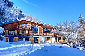 A large wooden house is surrounded by snow and trees