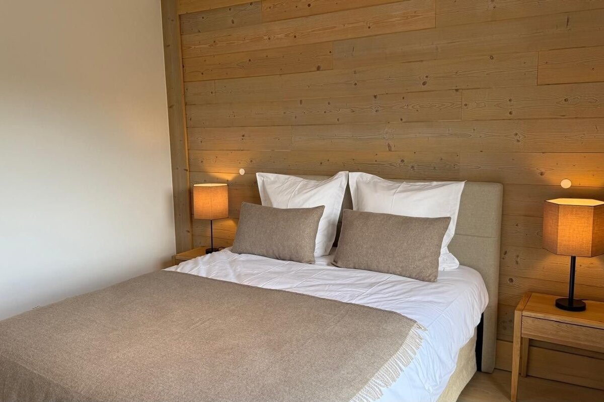 Cozy bedroom featuring a double bed with neutral linens, flanked by lit bedside lamps against a rustic wood-paneled wall.