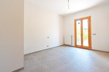 An empty room with white walls, grey tiled floor, a wooden French door, a radiator, and an exposed light bulb from the ceiling.