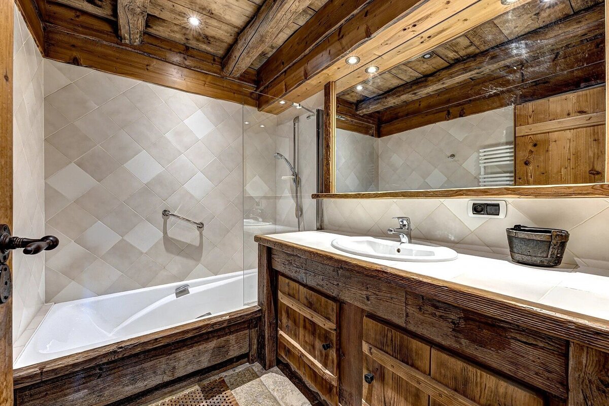 Cozy, rustic bathroom featuring exposed wooden beams, a wooden vanity, white diamond-tiled walls, a bathtub, and shower.