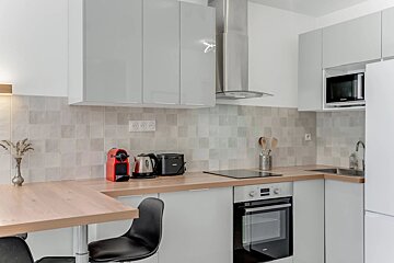 A modern white kitchen with grey cabinets, wood countertops, integrated appliances, and a small dining table.