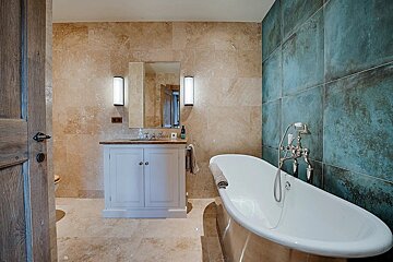 A well-appointed bathroom featuring a white freestanding bathtub, beige tiled walls, a striking blue-green accent wall, and a vanity with mirror.