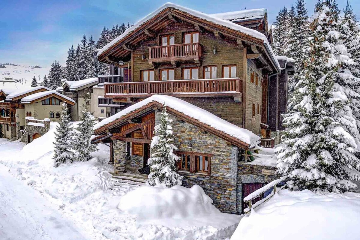 A large house with a balcony is surrounded by snow covered trees