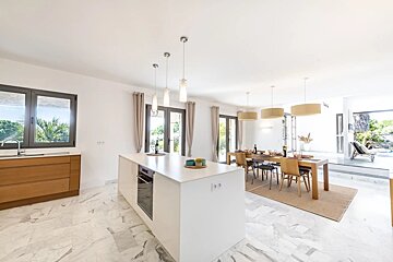 Bright, modern open-plan kitchen and dining area featuring marble floors, a white island, and a wooden dining table.