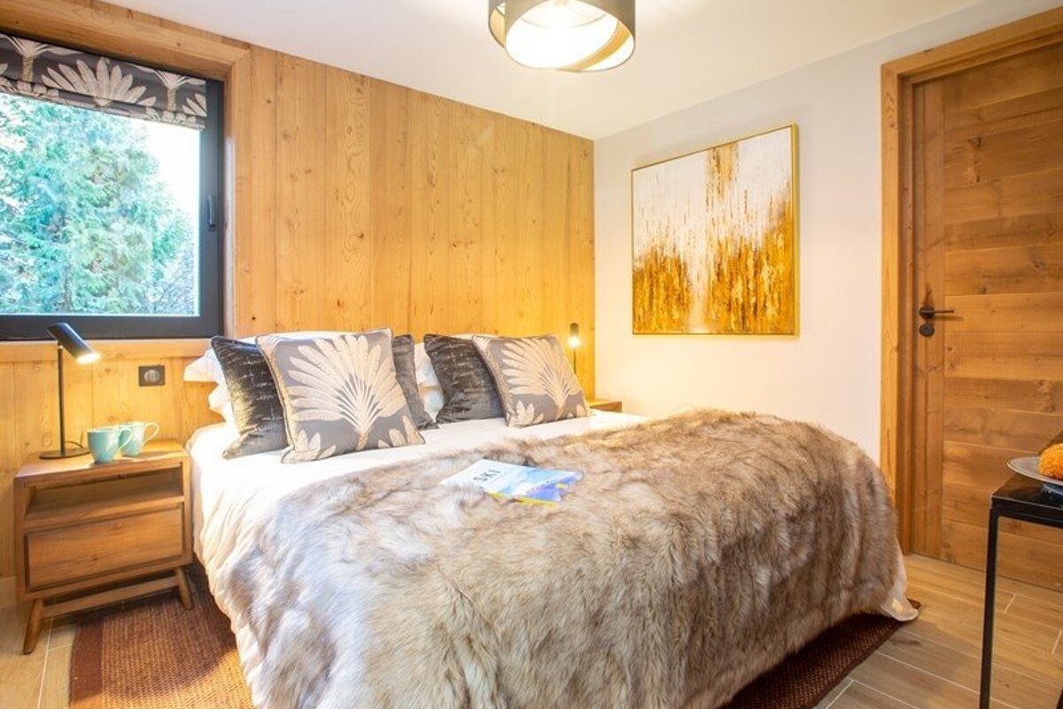 Cozy cabin bedroom featuring a bed with a faux fur throw, wood-paneled wall, patterned pillows, and abstract gold artwork.