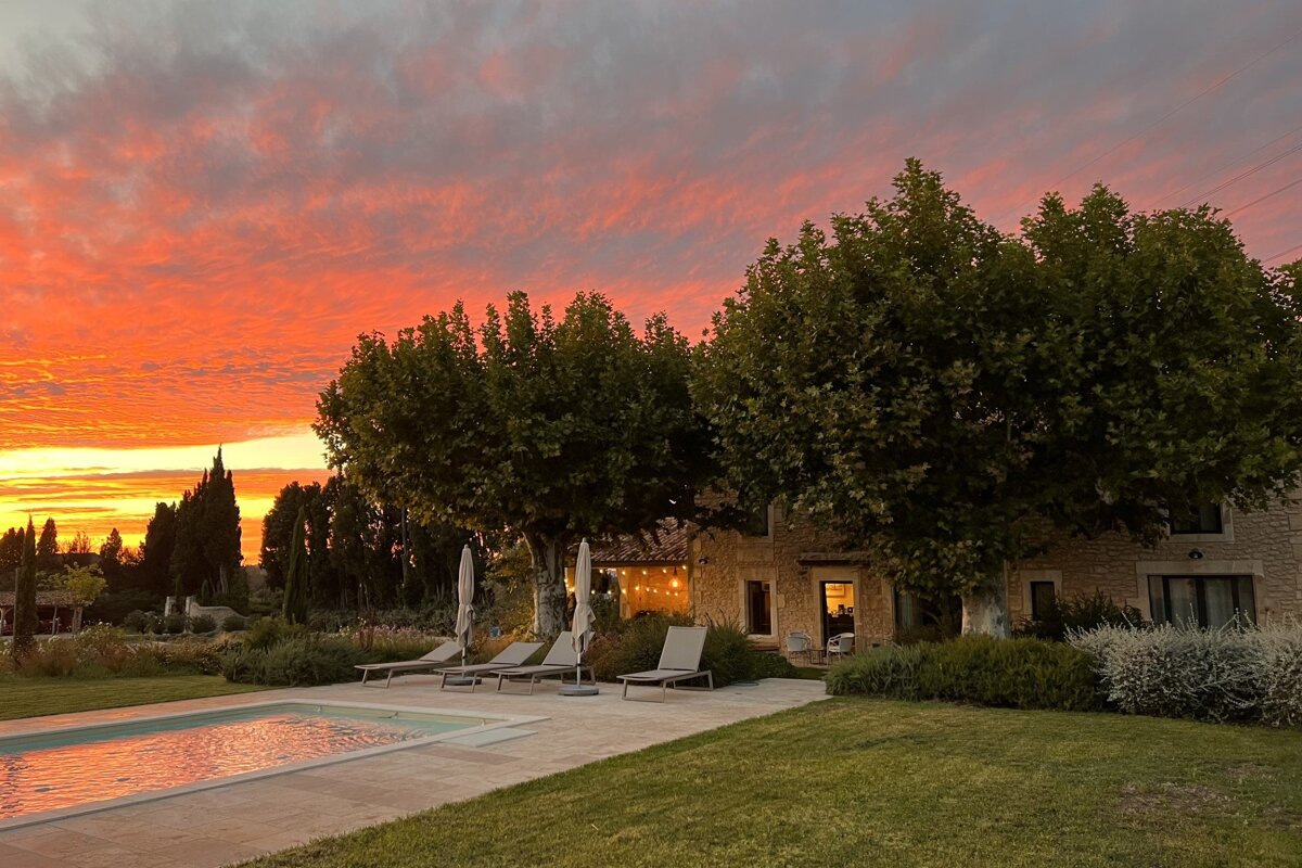 A sunset over a swimming pool with chairs and umbrellas