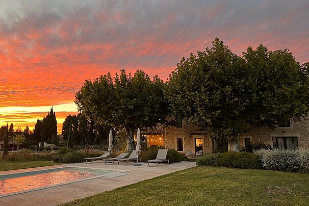 A sunset over a swimming pool with chairs and umbrellas