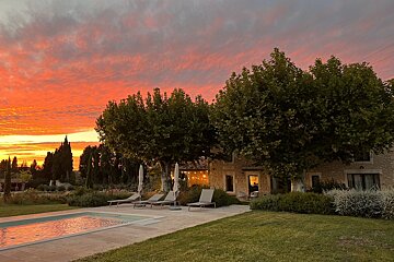 A sunset over a swimming pool with chairs and umbrellas