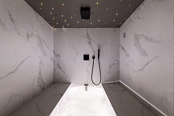 A bathroom with white tiles and a black shower head