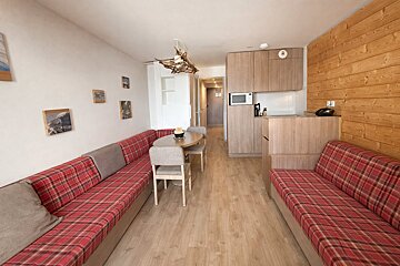 Cozy studio apartment with red plaid banquettes, a dining area, and a compact wooden kitchenette and accent wall.