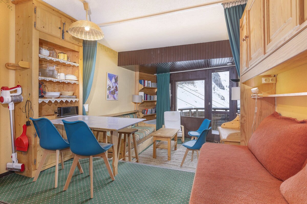 Cozy apartment living area with a dining table, built-in wooden furniture, green carpet, and a balcony showcasing snowy mountain views.
